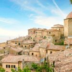 Vista panoramica del borgo toscano, con strade acciottolate e case in pietra circondate da colline verdi.
