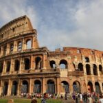 Turista deluso davanti al Colosseo in un giorno piovoso a Roma, evidenziando il clima sfavorevole.