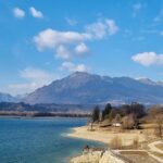 Vista panoramica del lago nascosto nel Friuli, circondato da montagne e vegetazione lussureggiante.