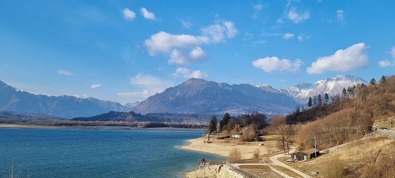Vista panoramica del lago nascosto nel Friuli, circondato da montagne e vegetazione lussureggiante.