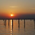 Tramonto sul paesaggio veneto con vigneti e calici di prosecco in primo piano.