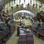 Bottega artigiana con prodotti tipici, artigiani al lavoro e clienti in visita.