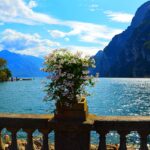 Panorama di un lago italiano in primavera, circondato da fiori colorati e montagne verdeggianti.