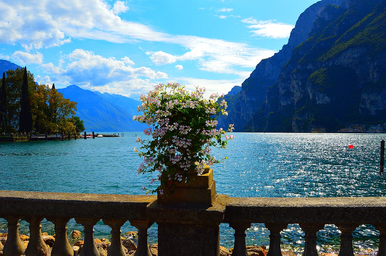 Panorama di un lago italiano in primavera, circondato da fiori colorati e montagne verdeggianti.