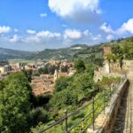Panorama mozzafiato del borgo piemontese con colline verdi e cielo sereno.