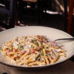 Pasta tipica veneta servita in un ristorante affollato da turisti entusiasti.