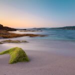 Spiaggia sarda all'alba, onde scintillanti e sabbia dorata brillano come diamanti sotto il sole nascente.