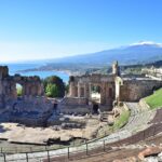 Panorama di un paese che evoca Catania, lontano dall'Etna, con architetture e paesaggi tipici.