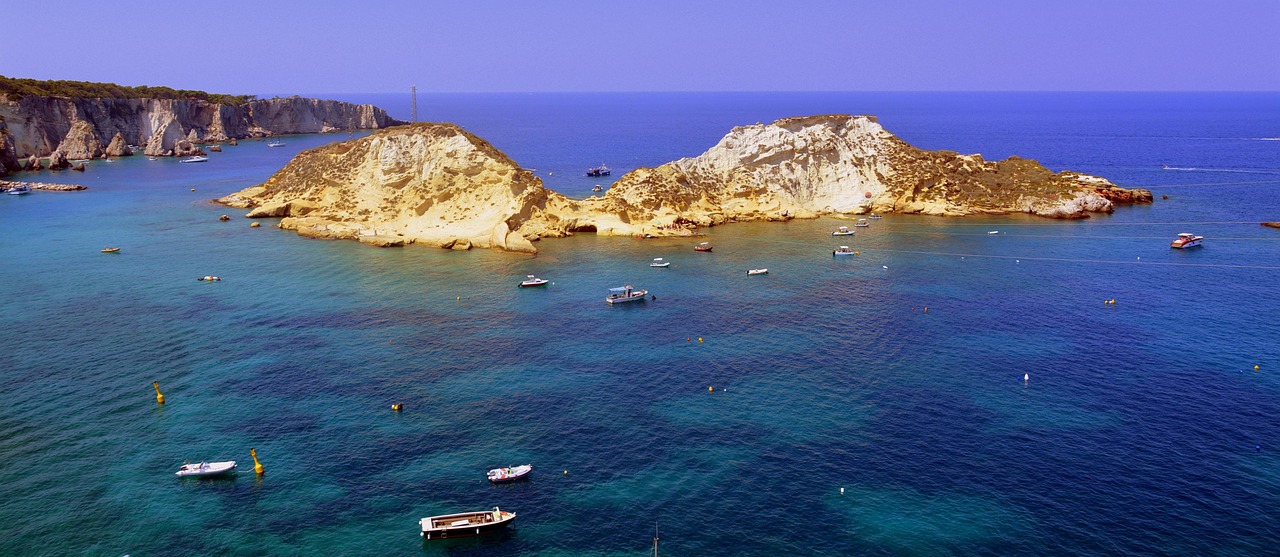 Spiaggia di Ponza con acque cristalline e sabbia bianca, circondata da scogliere verdi.