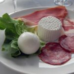 Mozzarella di bufala fresca su un tagliere, circondata da fattorie tradizionali in campagna campana.