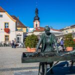 Piazza storica di un piccolo paese affollata durante un mercato locale vivace e colorato.